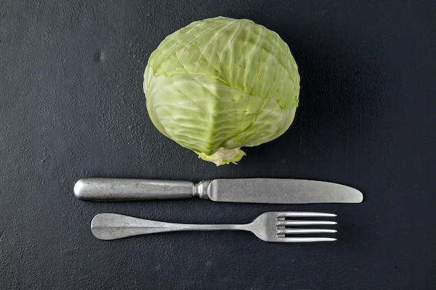 White cabbage and fork with knife on black concrete tabletop