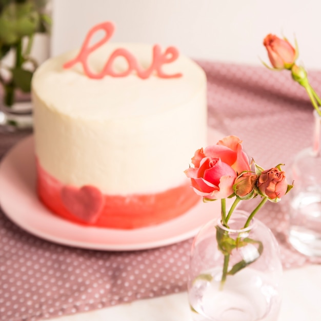 White cake with pink decor and the word love on top among small white and pink roses. Valentine's Day Gift Concept