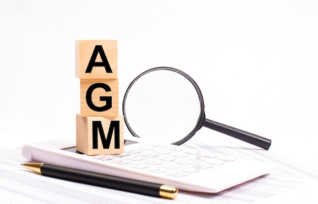 On a white calculator next to a magnifying glass and a black pen wooden cubes marked AGM stand upright