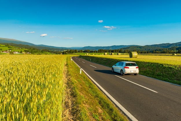 A white car drives between picturesque fields somewhere in Austria