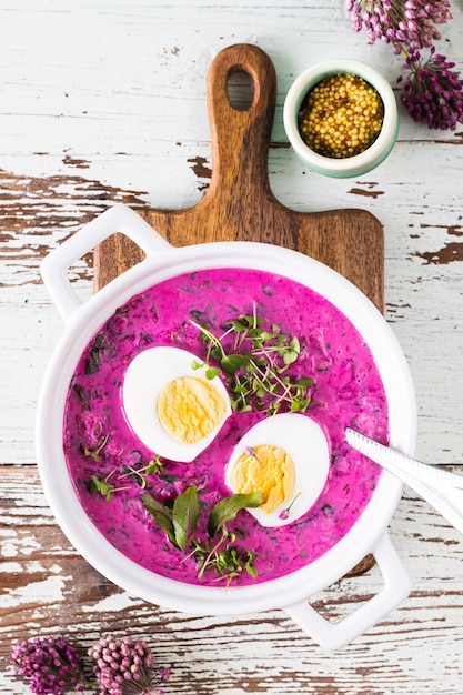 White casserole with cold summer beet cucumber and egg soup on a wooden table Top view