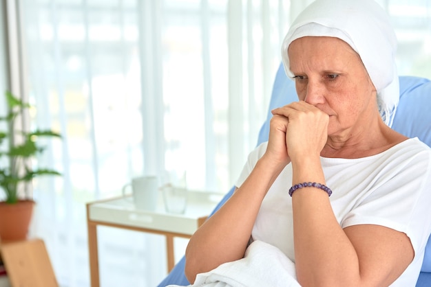 White caucasian female hairless and eyebrowless feel bad are praying and waiting for chemotherapy  in hospital room, breast cancer awareness month concept.