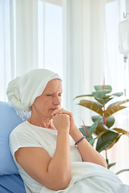 White caucasian female hairless and eyebrowless feel bad are praying and waiting for chemotherapy  in hospital room, breast cancer awareness month concept.