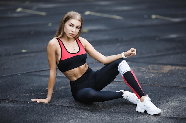 A white Caucasian girl in tight fitting fitness clothes stretches her muscles on a treadmill