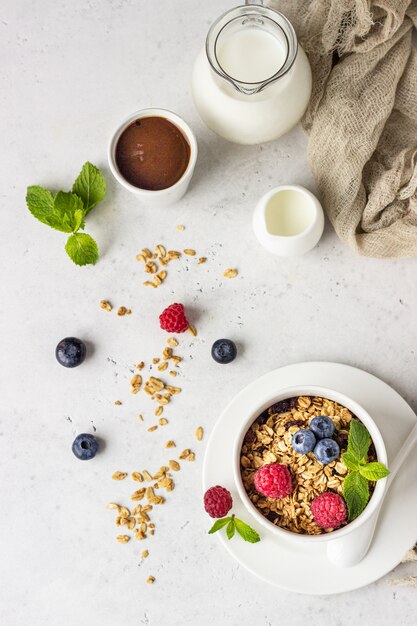 White ceramic bowl of homemade granola with milk, berries (blueberry and raspberry) and milk. Healthy breakfast ingredients. 