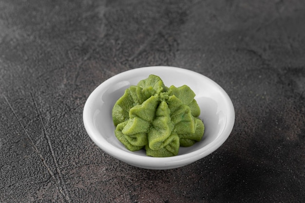 White ceramic bowl with a wasabi sauce for sushi dark gray textured background side view