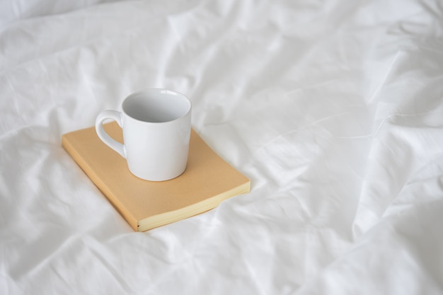 White ceramic coffee mug placed on Notebook brown cover.