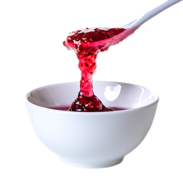 White ceramic spoon and bowl of blackberry jam isolated on white. Sweets.