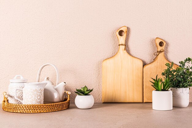 White ceramic tea set on round wicker tray among indoor plants on kitchen countertop Kitchen background in light colors A copy space Front view