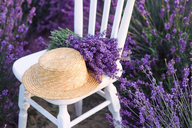 white chair with bouquet of lavender and straw hat at beautiful lavender flowers bloom.