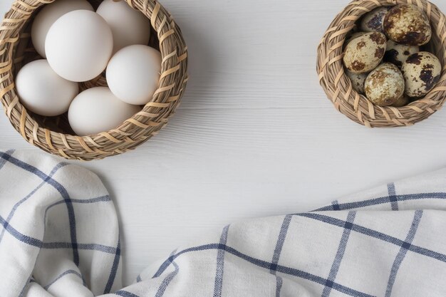 White chicken quail eggs in baskets and a towel on a white wooden background with space for text Easter holiday