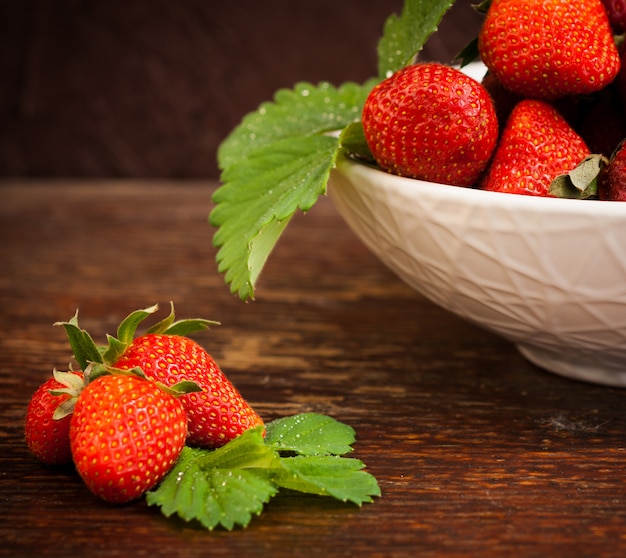 White china bowl filled with succulent juicy fresh ripe red strawberries on an old wooden textured table top