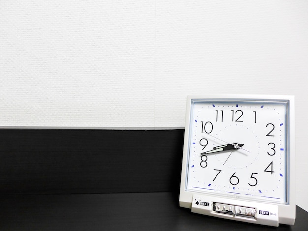 the white clock on the black shelf with white wall background