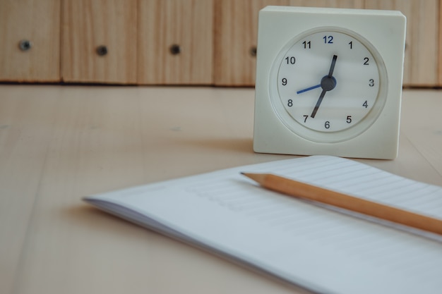 White clock put near Notebook and pencil