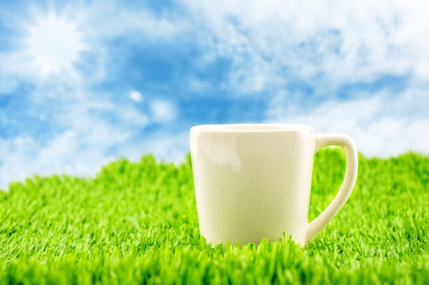 White coffee cup on green grass with blue sky and sunburst,Spring Season