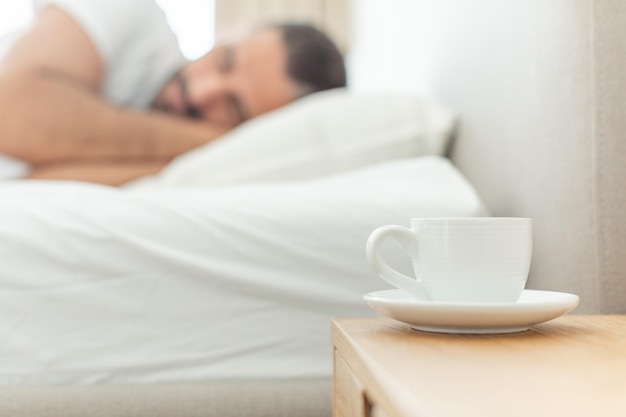 Photo white coffee cup rests on nightstand beside a sleeping man