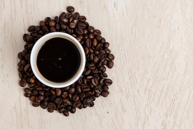 White coffee cup surrounded with beans on wooden table, top view