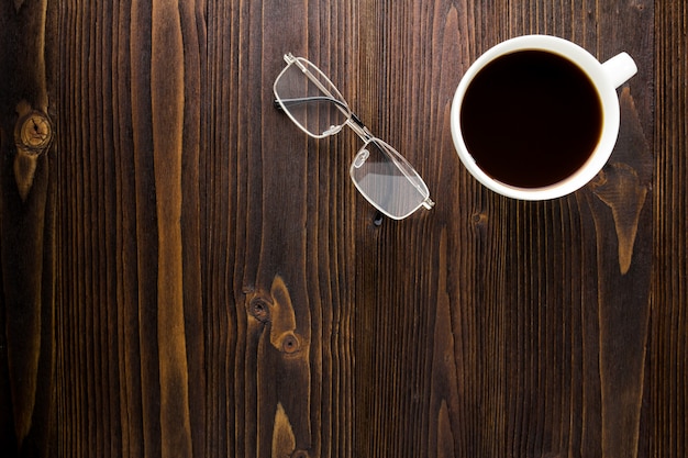 White coffee cup with black coffee and glasses on wooden table.