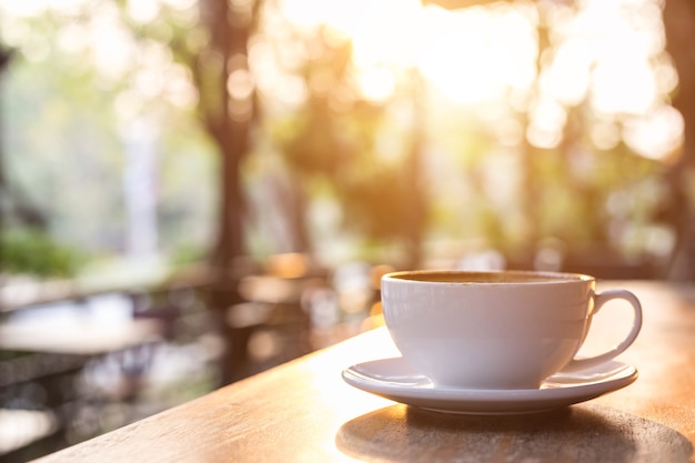 White coffee cup on wooden table or counter in coffee shop and blur light bokeh background