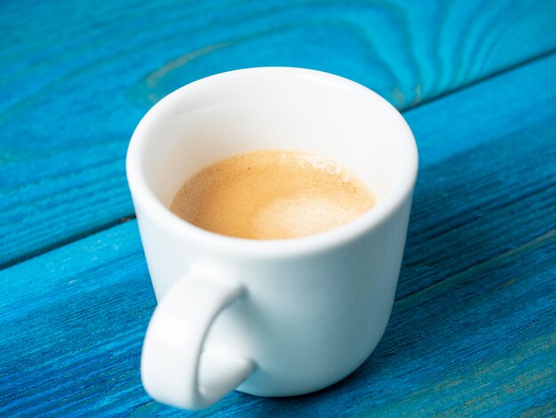 White coffee mug with poured espresso on a blue wooden background. Coffee, energy drink