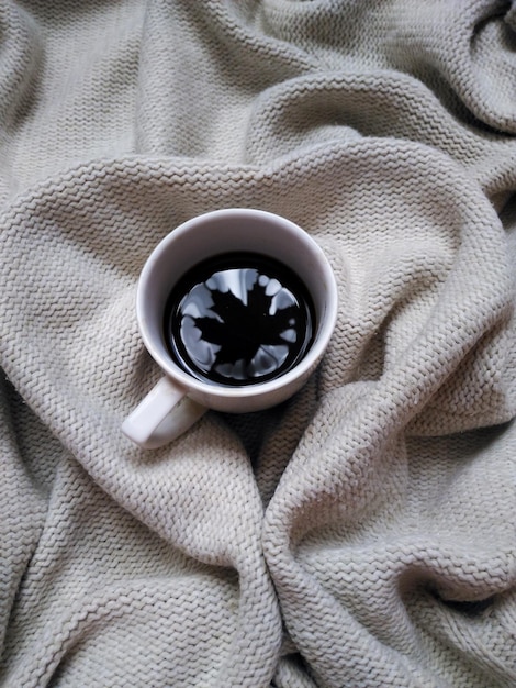 White coffee mug with wedge leaf reflection in the Cup. On beige knitted background.