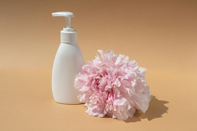 White cosmetic bottle and pink peony bud on brown background Skin hydration and health