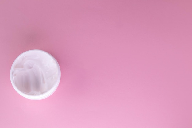 White cosmetic face cream in a round open jar on a pink background top view copy of the space on the right