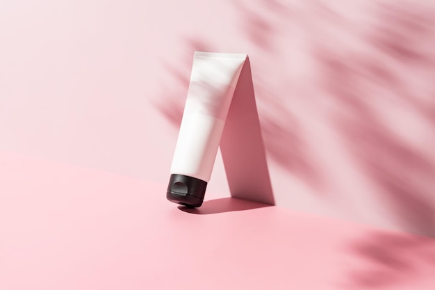 white cosmetic tube for face or body cream cleanser or shampoo on a pink background with leaves shadows Concept of minimalism in cosmetic packaging Copy space