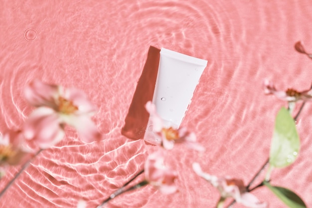 White cosmetic tube on the pink water surface Blank label for branding mockup Flat lay top view