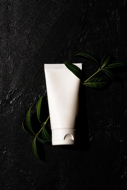 white cosmetic tube with hand cream on a dark background with green leaves Cosmetics concept with herbal ingredients