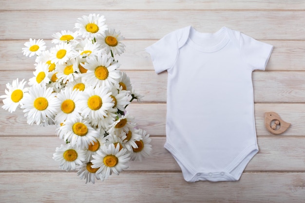 White cotton baby short sleeve onesie mockup with wild daisy flowers and wooden baby bird toy Design gender neutral bodysuit template newborn romper print presentation mock up