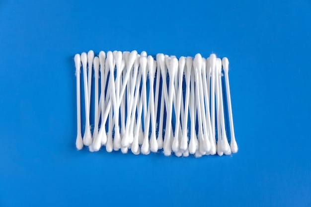 White cotton buds are collected side by side and lie in the center on a blue background.