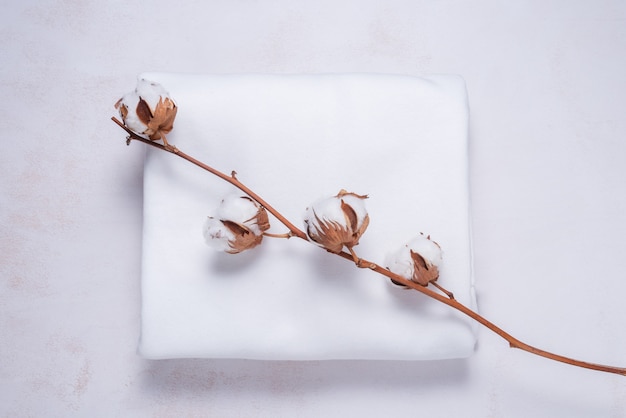 White cotton fabric with cotton flower branch on wooden background