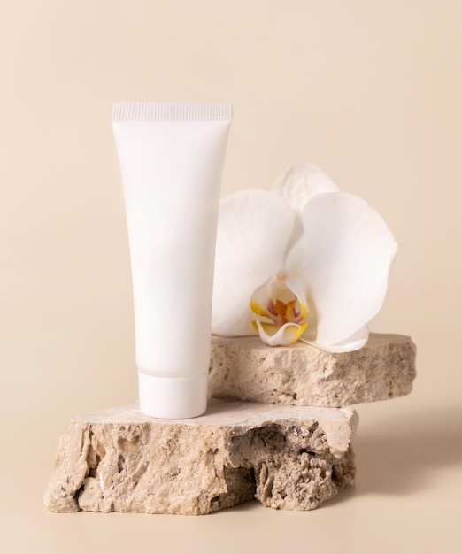 White cream tube near white orchid flower on light yellow Mockup Skincare product