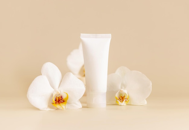 White cream tube near white orchid flowers on light beige close up Mockup Skincare product