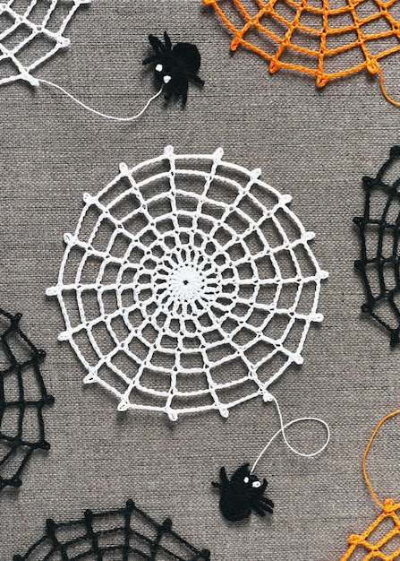 White crochet spider web on nature linen background with small funny black spaders