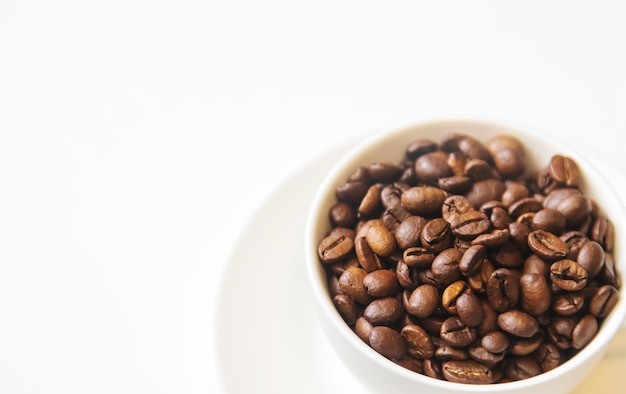 White cup and coffee beans on a white background. Selective focus.