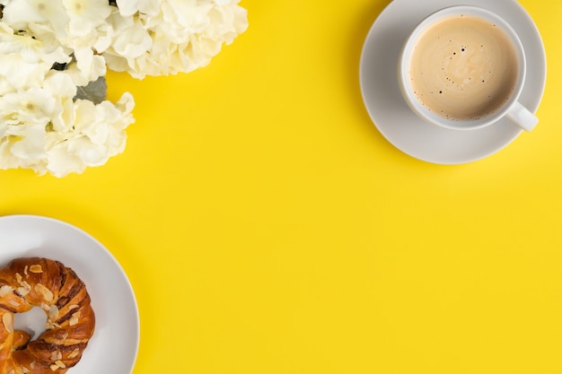 White cup of coffee and flowers on yellow background. Flat lay top view breakfast concept