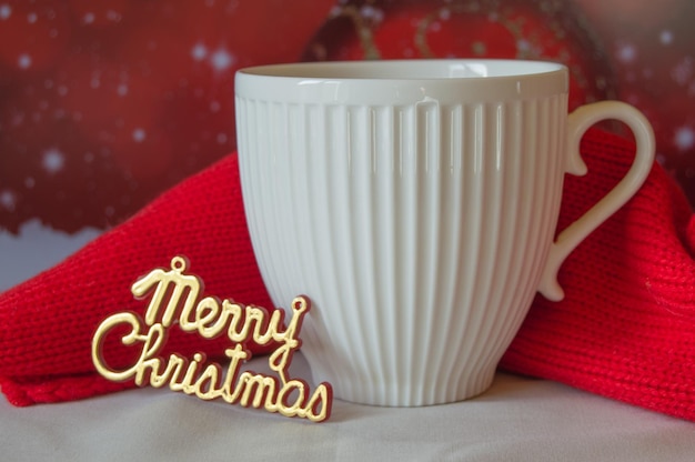 White Cup of coffee and a knitted red scarf the words Merry Christmas