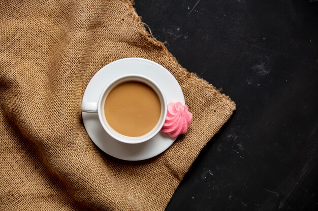 White cup of coffee and meringue on dark background