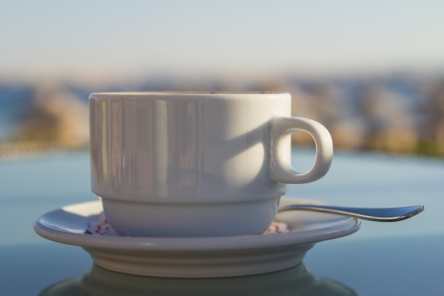 White cup of coffee on the table at sea. Summer holiday concept