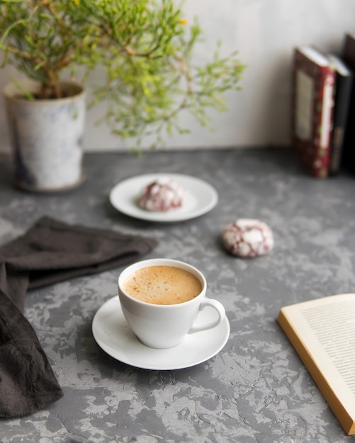 White cup of coffee with green houseplant and open book