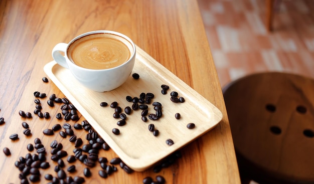 White cup of espresso coffee and Roasted coffee beans on wooden counter at coffee shop