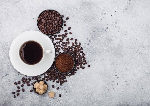 White cup of fresh raw organic coffee with beans and ground powder with cane sugar cubes with coffee tree leaf on light background. Top view