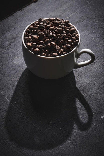 White cup of freshly brewed roasted coffee beans on gray background