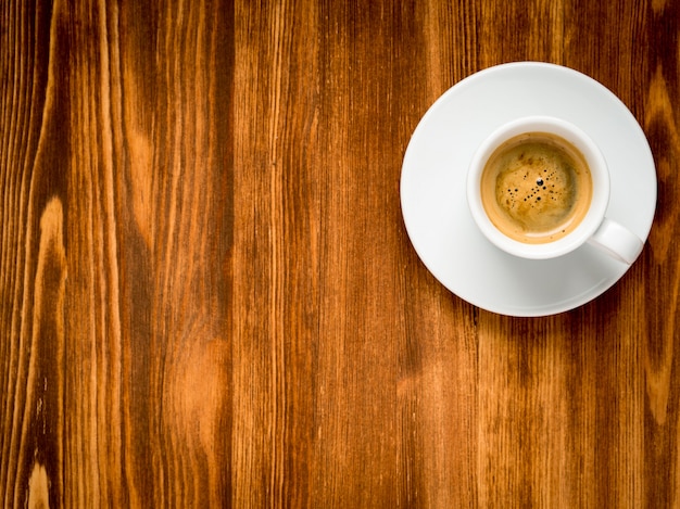 White cup of frothy coffee on brown dark wooden background. Top view with vignette