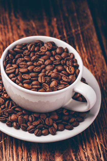 White cup full of roasted coffee beans on saucer