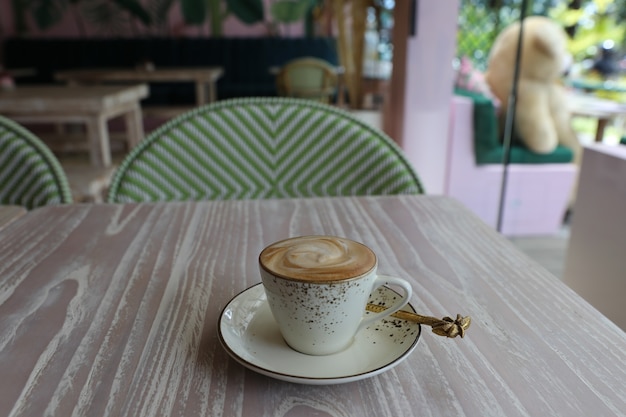 White cup of hot cappuccino on wooden light table background.