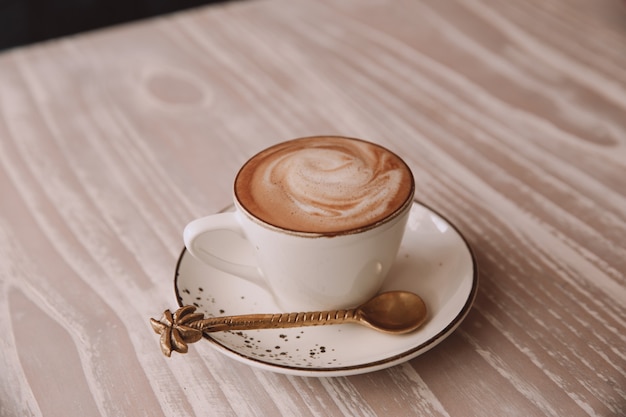 White cup of hot cappuccino on wooden light table background.