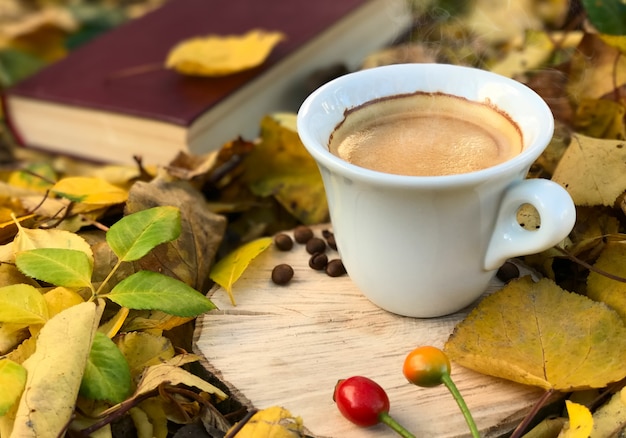 White cup of hot coffee among fallen autumn leaves 